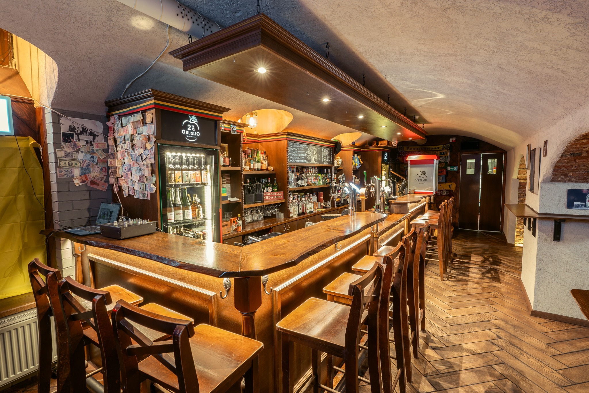 Medinis rūsio baras su aukštomis kėdėmis, ilgu baro stalviršiu ir gėrimų lentynomis